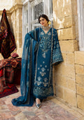 Woman in a blue embroidered traditional outfit standing in front of a stone wall.