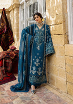Woman in a blue embroidered traditional outfit standing in front of a stone wall.