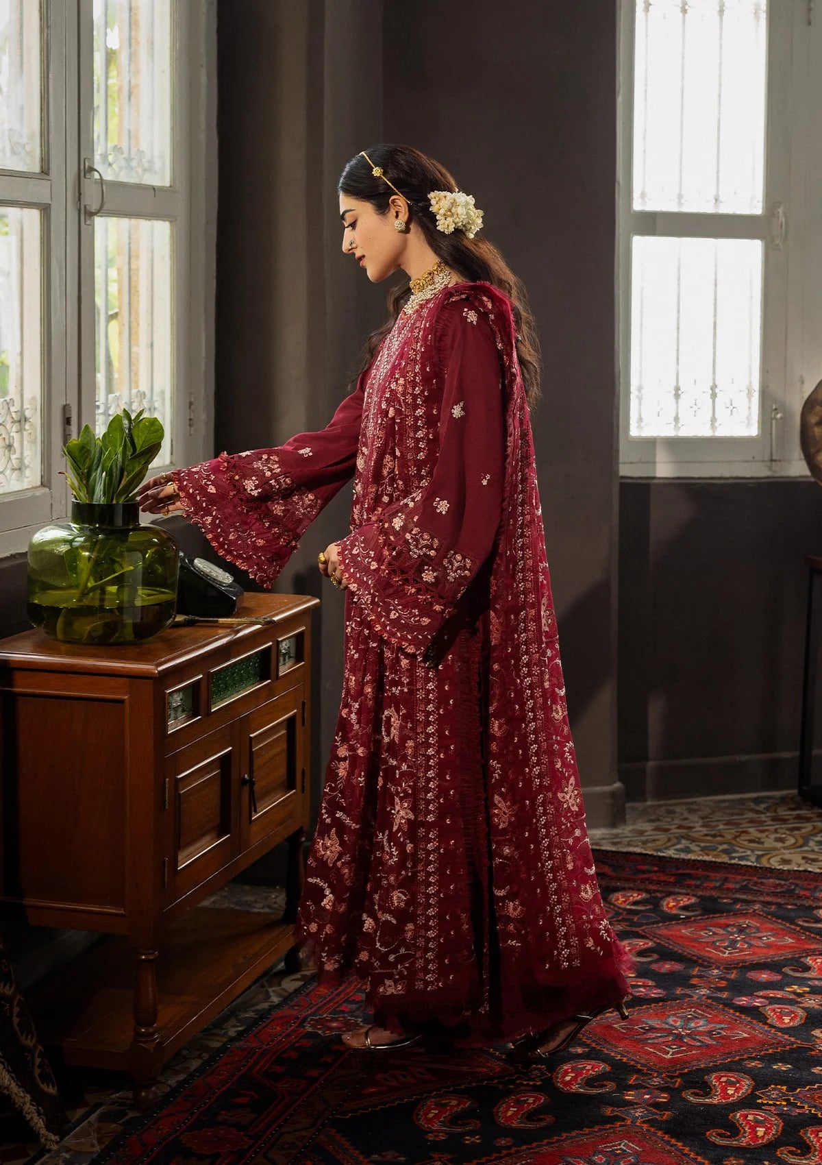 Woman in a red floral dress standing in a room with dark walls and a patterned rug.